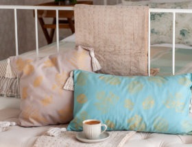 Dwie poduszki malowane w złote liście z chwostami leżące na tapicerowanej ławce w sypialni.