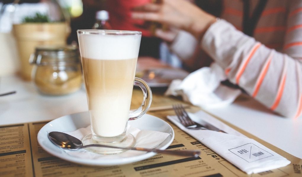 Kawa latte w wysokiej szklance z łyżeczką stoi na stoliku.