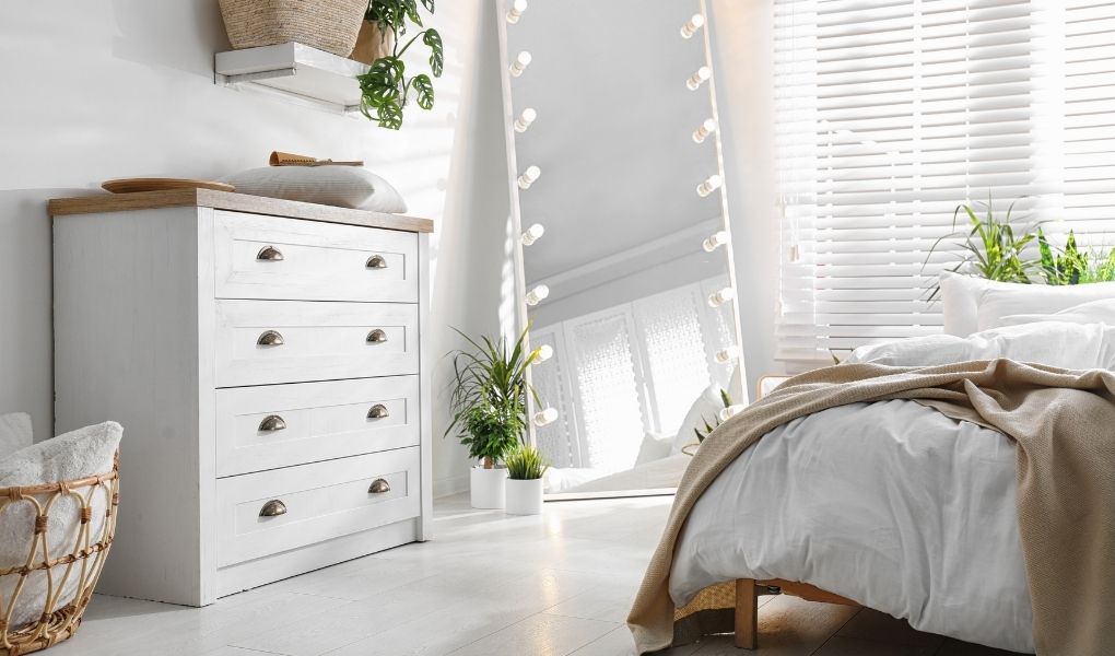 Biała nowoczesna komoda z szufladami stoi w sypialni urządzonej w bieli.