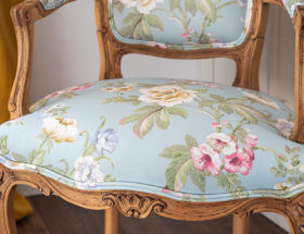 Fragment krzesła ludwik w nowym obiciu w pastelowe kwiaty wykończonym podwójna lamówką tapicerską.