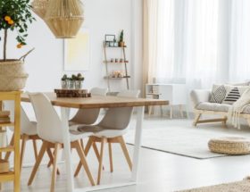 Stół z drewnianym blatem i krzesłami stoi w salonie urządzonym w jasnych kolorach.