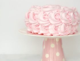 Tort udekorowany różowym kremem stoi na różowej paterze w białe grochy.
