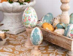 Wielkanocne pisanki ze styropianowych jajek ozdobionych kolorowymi tkaninami stoją na drewnianych podstawkach.