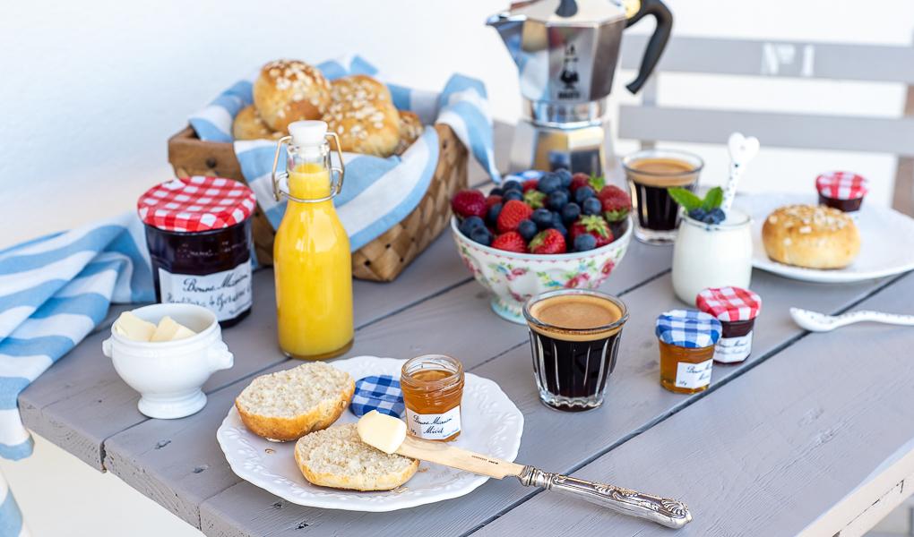 Na blacie stolika stoi śniadanie z bułeczkami na drożdżach, czarną kawą, sokiem pomarańczowym i owocami.