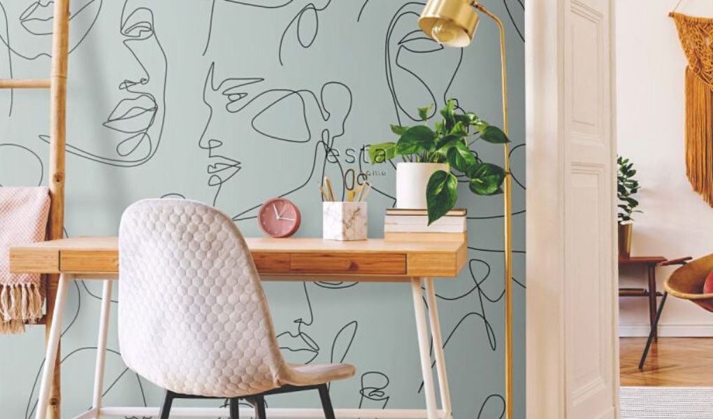 Biurko stoi przy ścianie pokrytej nowoczesną tapetą w abstrakcyjny wzór.