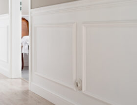 Fragment ściany w korytarzu ozdobionej białymi listwami dekoracyjnymi i ceramicznym gniazdkiem retro.