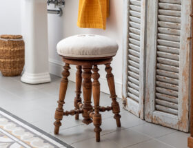Stary stołek do pianina obity kremowym lnem stoi w łazience w stylu retro.