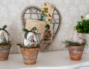 Wielkanocne dekoracje ze starymi doniczkami, jajkami i kurką stoją na białym blacie.